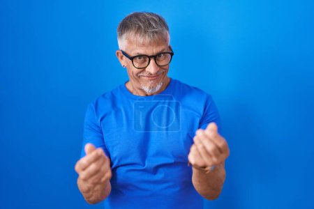 Téléchargez les photos : Homme hispanique avec les cheveux gris debout sur fond bleu faisant geste d'argent avec les mains, demandant le paiement du salaire, entreprise millionnaire - en image libre de droit