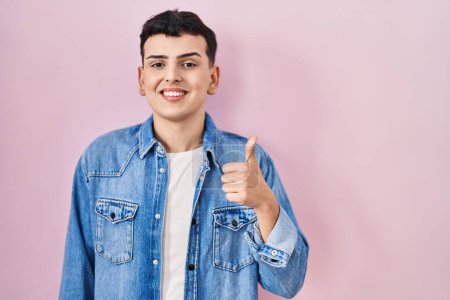 Photo for Non binary person standing over pink background smiling happy and positive, thumb up doing excellent and approval sign - Royalty Free Image