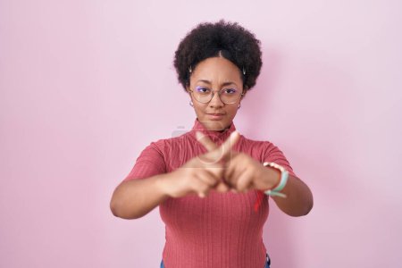 Photo for Beautiful african woman with curly hair standing over pink background rejection expression crossing fingers doing negative sign - Royalty Free Image