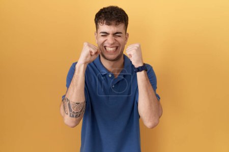 Photo for Young hispanic man standing over yellow background excited for success with arms raised and eyes closed celebrating victory smiling. winner concept. - Royalty Free Image