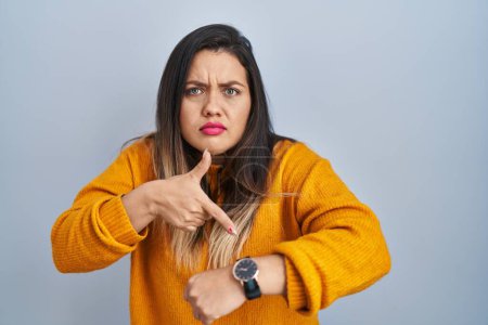 Téléchargez les photos : Young hispanic woman standing over isolated background in hurry pointing to watch time, impatience, upset and angry for deadline delay - en image libre de droit