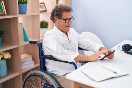 Téléchargez les photos : Homme d'âge moyen utilisant smartphone assis sur fauteuil roulant télétravail à la maison - en image libre de droit
