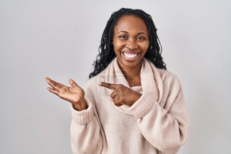 Téléchargez les photos : Femme africaine debout sur fond blanc étonné et souriant à la caméra tout en présentant avec la main et pointant du doigt. - en image libre de droit