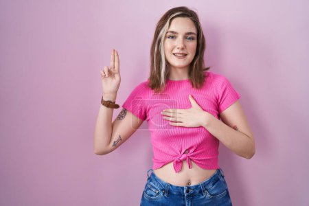 Foto de Blonde caucasian woman standing over pink background smiling swearing with hand on chest and fingers up, making a loyalty promise oath - Imagen libre de derechos