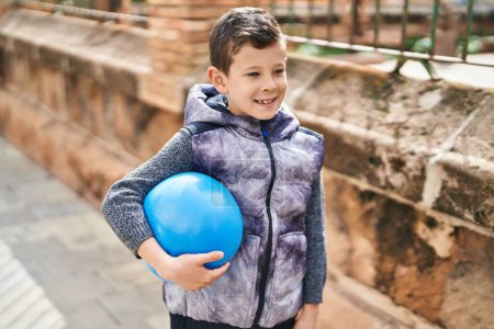 Foto de Niño rubio sonriendo confiado sosteniendo la pelota en la calle - Imagen libre de derechos