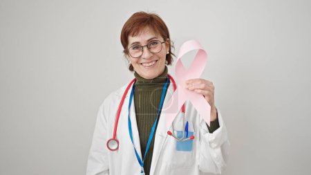 Photo for Mature hispanic woman doctor holding breast cancer awareness pink ribbon over isolated white background - Royalty Free Image
