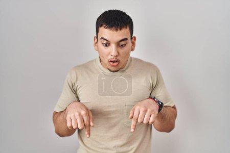 Téléchargez les photos : Jeune homme arabe portant t-shirt décontracté pointant vers le bas avec les doigts montrant la publicité, visage surpris et bouche ouverte - en image libre de droit