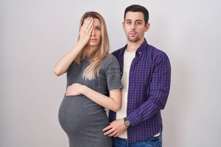 Photo for Young couple expecting a baby standing over white background yawning tired covering half face, eye and mouth with hand. face hurts in pain. - Royalty Free Image