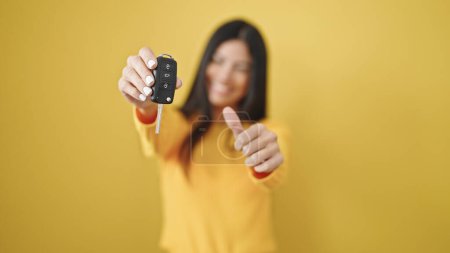 Photo for Young beautiful hispanic woman pointing to key of new car doing ok gesture over isolated yellow background - Royalty Free Image
