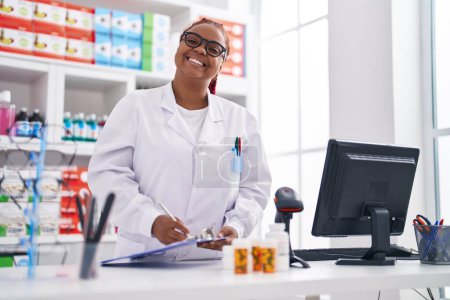 Téléchargez les photos : African american woman pharmacist writing on checklist at pharmacy - en image libre de droit