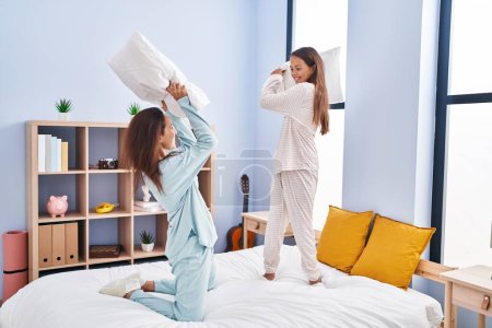 Foto de Woman and girl mother and daughter fighting with pillow on bed at bedroom - Imagen libre de derechos
