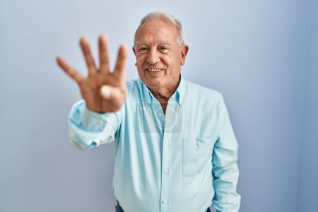 Téléchargez les photos : Homme âgé avec les cheveux gris debout sur fond bleu montrant et pointant vers le haut avec les doigts numéro quatre tout en souriant confiant et heureux. - en image libre de droit