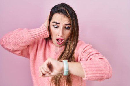 Téléchargez les photos : Jeune femme hispanique debout sur fond rose regardant le temps de la montre inquiet, peur de se faire tard - en image libre de droit