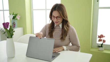 Photo for Young beautiful hispanic woman using laptop sitting on table at home - Royalty Free Image