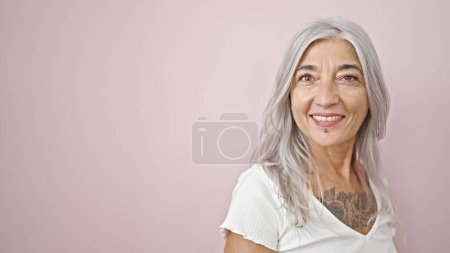 Téléchargez les photos : Femme aux cheveux gris d'âge moyen souriant confiante debout sur fond rose isolé - en image libre de droit