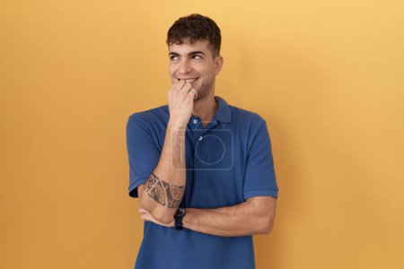 Photo for Young hispanic man standing over yellow background with hand on chin thinking about question, pensive expression. smiling and thoughtful face. doubt concept. - Royalty Free Image