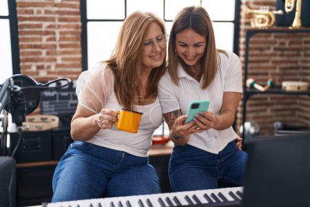 Photo for Mother and daughter musicians using smartphone drinking coffee at music studio - Royalty Free Image