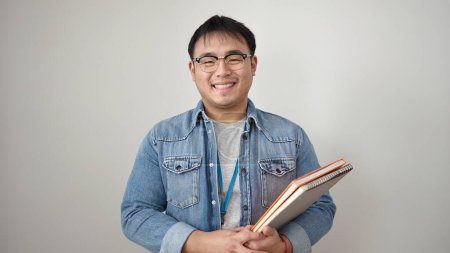 Foto de Joven hombre chino sonriendo confiado sosteniendo libros sobre fondo blanco aislado - Imagen libre de derechos