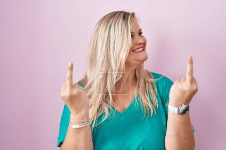 Foto de Caucasian plus size woman standing over pink background showing middle finger doing fuck you bad expression, provocation and rude attitude. screaming excited - Imagen libre de derechos