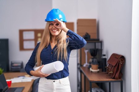 Photo for Young woman wearing architect hardhat smiling happy doing ok sign with hand on eye looking through fingers - Royalty Free Image