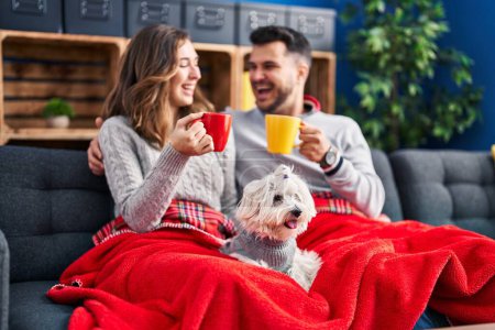 Photo for Man and woman drinking coffee sitting on sofa with dog at home - Royalty Free Image