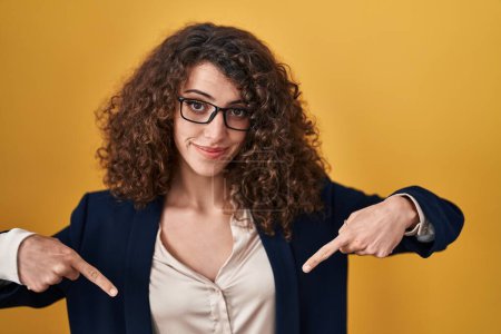 Photo for Hispanic woman with curly hair standing over yellow background looking confident with smile on face, pointing oneself with fingers proud and happy. - Royalty Free Image
