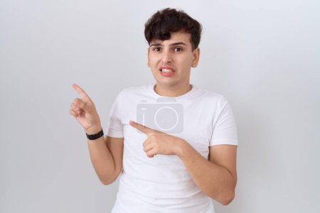 Téléchargez les photos : Jeune homme non binaire portant un t-shirt blanc décontracté pointant de côté inquiet et nerveux avec les deux mains, préoccupé et expression surprise - en image libre de droit