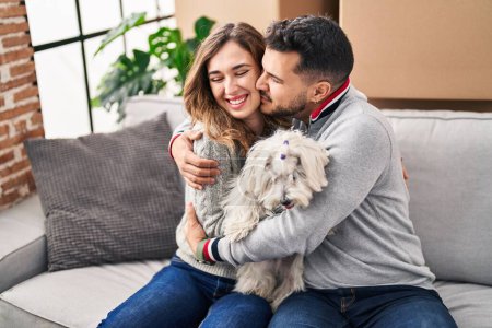 Foto de Hombre y mujer sonriendo confiados sentados en sofá con perro en casa nueva - Imagen libre de derechos