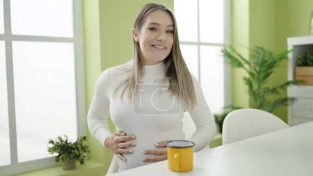 Téléchargez les photos : Jeune femme enceinte buvant du café assis sur la table parlant à la salle à manger - en image libre de droit