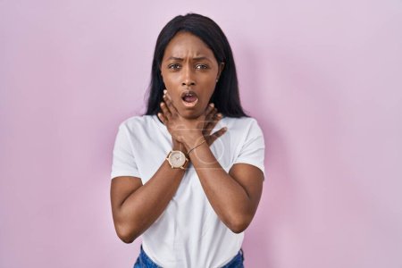 Foto de Mujer joven africana con camiseta blanca casual gritando sofocado porque estrangulamiento doloroso. problema de salud. concepto de asfixia y suicidio. - Imagen libre de derechos
