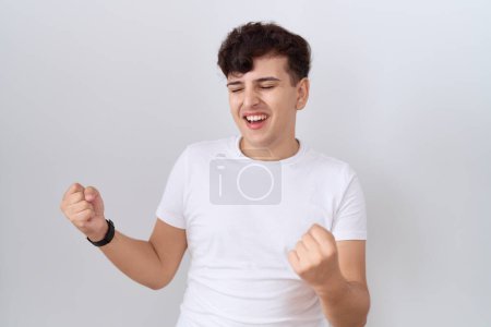 Téléchargez les photos : Jeune homme non binaire portant t-shirt blanc décontracté très heureux et excité faire geste gagnant avec les bras levés, souriant et criant pour le succès. concept de célébration. - en image libre de droit