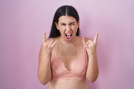 Photo for Young hispanic woman wearing pink bra shouting with crazy expression doing rock symbol with hands up. music star. heavy music concept. - Royalty Free Image