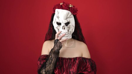 Téléchargez les photos : Jeune femme chinoise portant katrina costume tenant masque de crâne sur fond rouge isolé - en image libre de droit