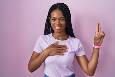 Téléchargez les photos : Femme afro-américaine avec des tresses debout sur fond rose souriant jurant avec la main sur la poitrine et les doigts vers le haut, faisant un serment de fidélité - en image libre de droit