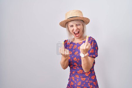Foto de Young caucasian woman wearing flowers dress and summer hat showing middle finger doing fuck you bad expression, provocation and rude attitude. screaming excited - Imagen libre de derechos