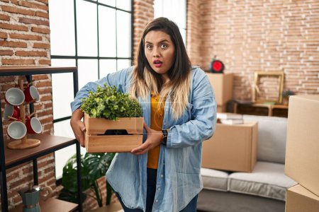 Photo for Young hispanic woman moving to a new home holding plants scared and amazed with open mouth for surprise, disbelief face - Royalty Free Image
