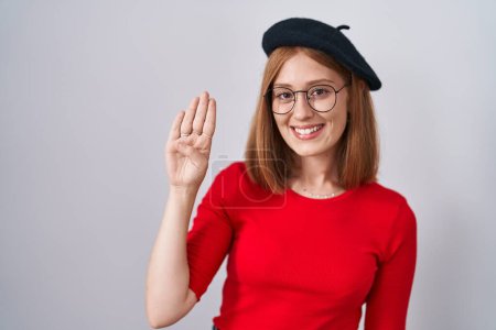 Téléchargez les photos : Jeune rousse femme debout portant des lunettes et un béret montrant et pointant vers le haut avec les doigts numéro quatre tout en souriant confiant et heureux. - en image libre de droit