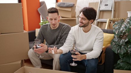 Photo for Two men couple drinking glass of wine at new home - Royalty Free Image