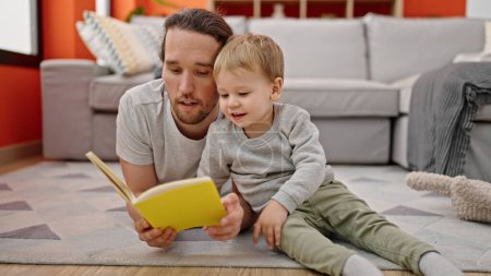 Téléchargez les photos : Père et fils lisant le livre assis ensemble sur le sol à la maison - en image libre de droit