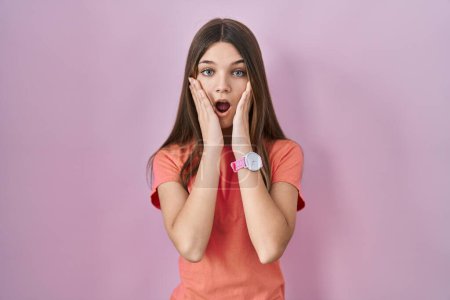 Photo for Teenager girl standing over pink background afraid and shocked, surprise and amazed expression with hands on face - Royalty Free Image
