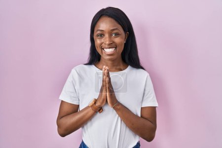 Photo for African young woman wearing casual white t shirt praying with hands together asking for forgiveness smiling confident. - Royalty Free Image