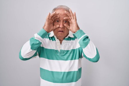 Téléchargez les photos : Homme âgé avec les cheveux gris debout sur fond blanc essayant d'ouvrir les yeux avec les doigts, somnolent et fatigué pour la fatigue matinale - en image libre de droit