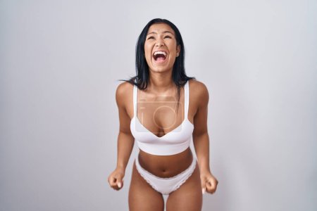 Foto de Hispanic woman wearing lingerie angry and mad screaming frustrated and furious, shouting with anger. rage and aggressive concept. - Imagen libre de derechos