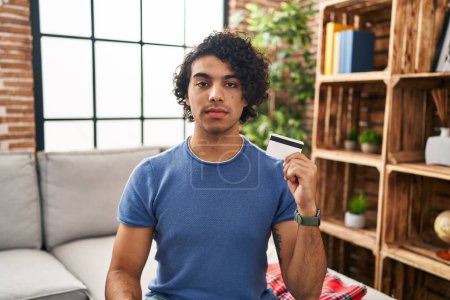 Photo for Hispanic man with curly hair holding credit card thinking attitude and sober expression looking self confident - Royalty Free Image