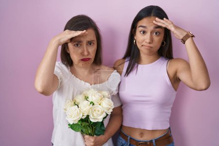 Téléchargez les photos : Mère et fille hispaniques tenant un bouquet de fleurs blanches inquiètes et stressées par un problème avec la main sur le front, nerveuses et anxieuses de crise - en image libre de droit