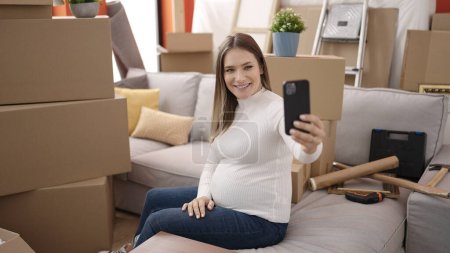 Photo for Young pregnant woman having video call sitting on sofa at new home - Royalty Free Image