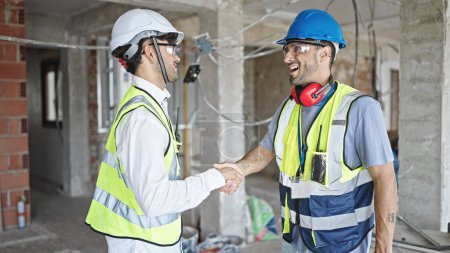 Foto de Dos hombres constructores sonriendo confiados estrechan las manos en el sitio de construcción - Imagen libre de derechos