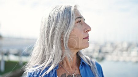 Téléchargez les photos : Femme aux cheveux gris d'âge moyen regardant vers le côté avec une expression sérieuse au bord de la mer - en image libre de droit