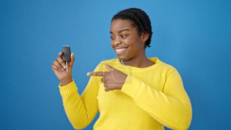 Photo for African american woman smiling confident pointing to key of new car over isolated blue background - Royalty Free Image