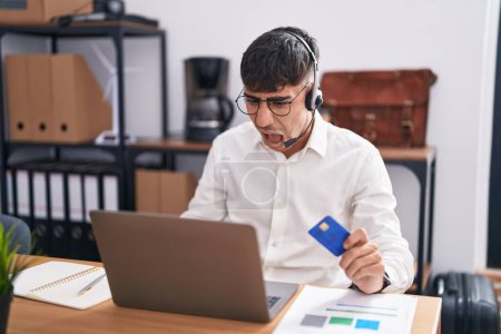 Photo for Young hispanic man working using computer laptop holding credit card angry and mad screaming frustrated and furious, shouting with anger. rage and aggressive concept. - Royalty Free Image